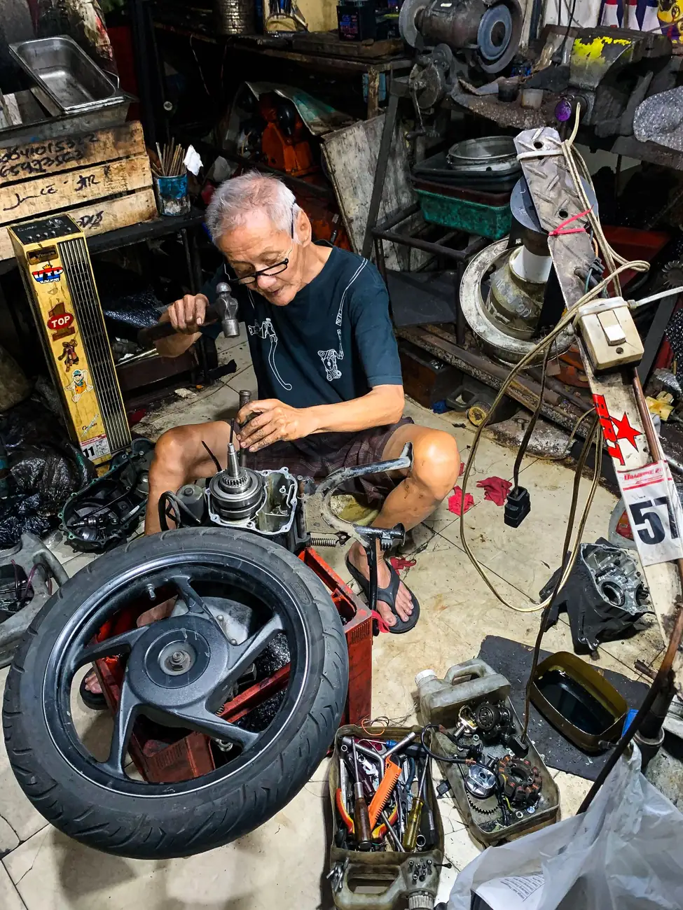 Người thợ lớn tuổi ngồi giữa đống phụ tùng xe máy